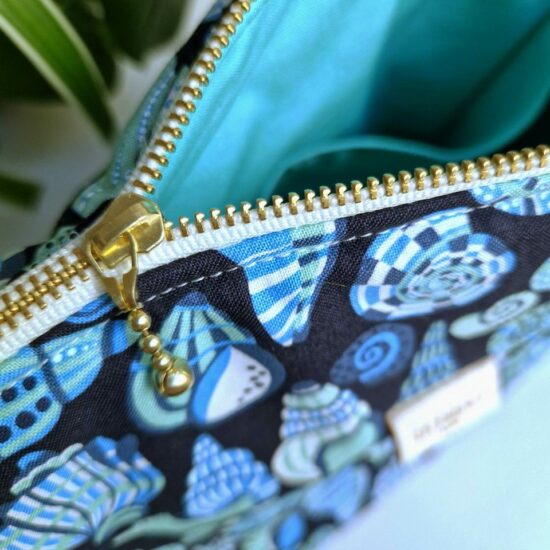 Jolie finition pour cette trousse de voyage ou de toilette doublure en coton bleu aqua poches interieures joli zip curseur billes dorées ruban zip blanc détails et finitions soignées fabrication française